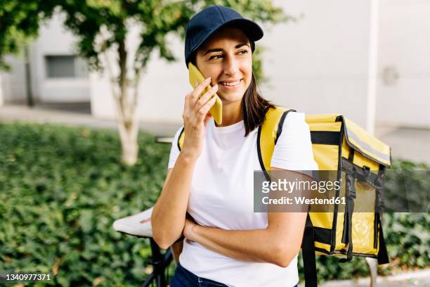 smiling essential service woman with delivery backpack talking on mobile phone - essenzielle berufe und dienstleistungen stock-fotos und bilder