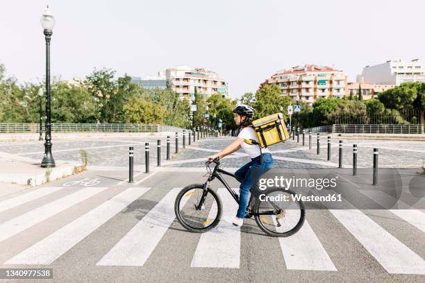 delivery woman carrying courier bag while riding bicycle on road - bicycle messenger stock-fotos und bilder