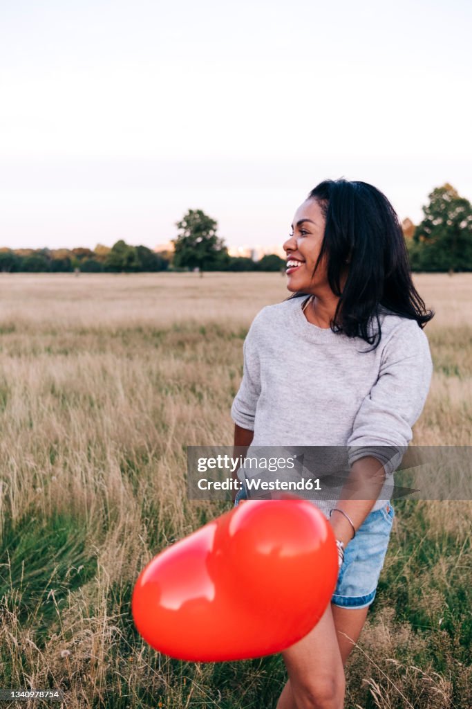 Cheerful woman with balloon walking on grass