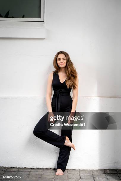 young woman standing on one leg in front of wall - jumpsuit stock-fotos und bilder