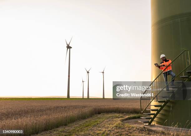 male inspector using digital tablet while standing on wind turbine staircase - green economy stock pictures, royalty-free photos & images