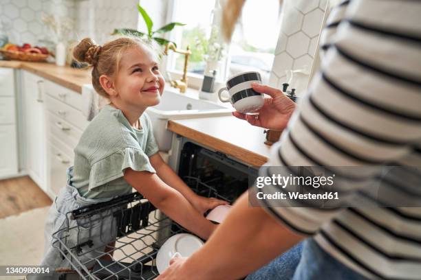 daughter helping mother arranging crockery in dishwasher - lave-vaisselle photos et images de collection