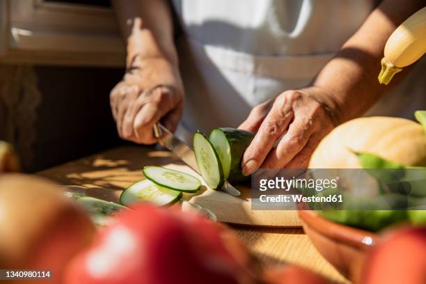 senior woman cutting cucumber in kitchen - gurke stock-fotos und bilder