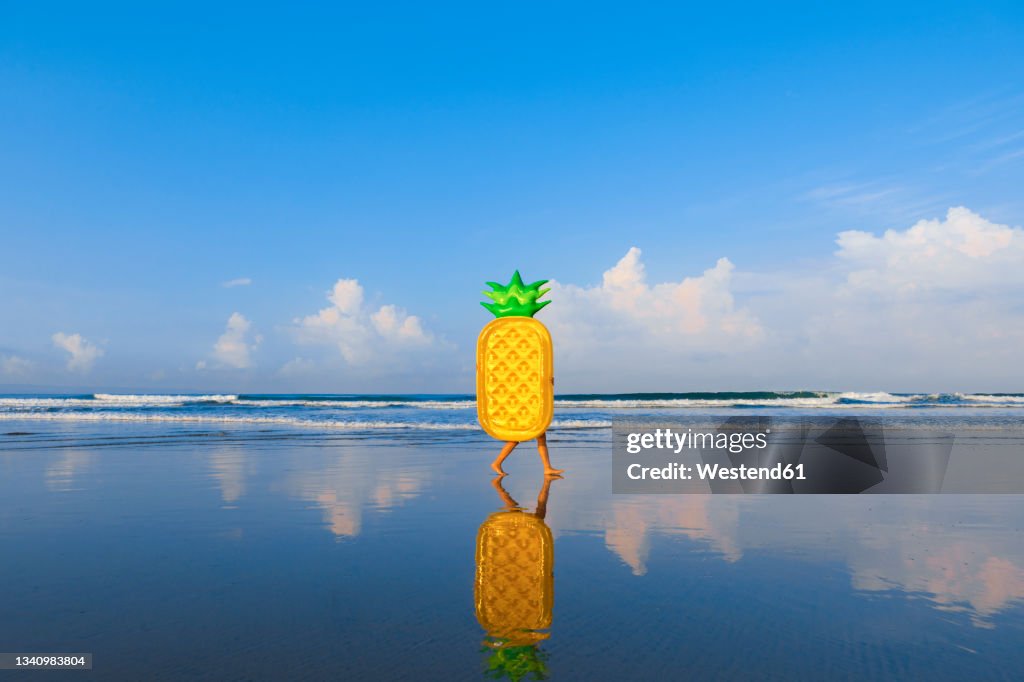 Woman with pineapple float walking at beach