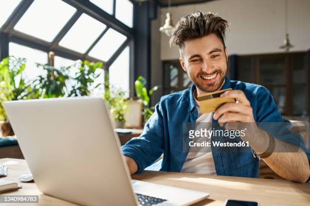 young businessman paying through credit card while using laptop in office - business man sitting banking ストックフォトと画像