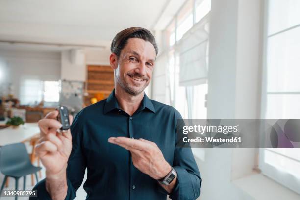 smiling businessman showing car key in office - mann stolz stock-fotos und bilder