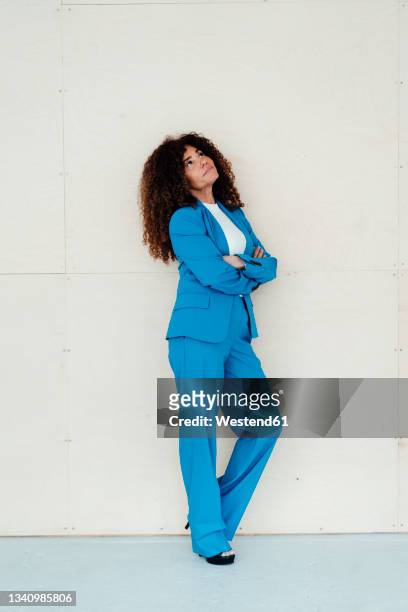 thoughtful female professional with arms crossed standing in front of wall - woman looking up sideview stock-fotos und bilder