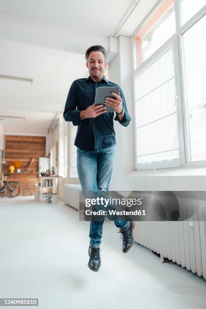 happy businessman using digital tablet while jumping in office - floating stock pictures, royalty-free photos & images