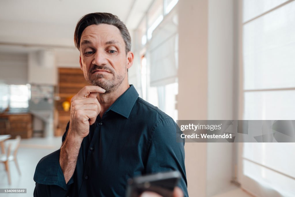 Confused businessman looking at smart phone in office