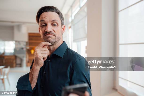 confused businessman looking at smart phone in office - portrait of business man looking surprised stock-fotos und bilder