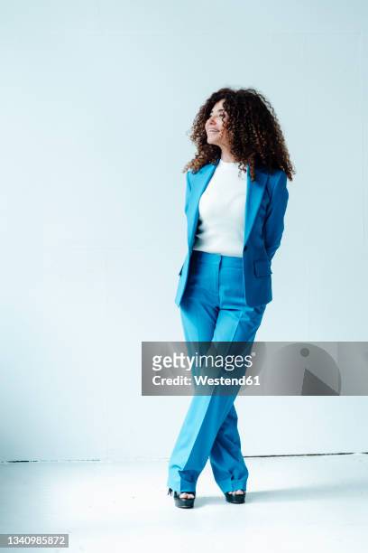 female professional with curly hair standing in front of wall - blue blazer stock pictures, royalty-free photos & images