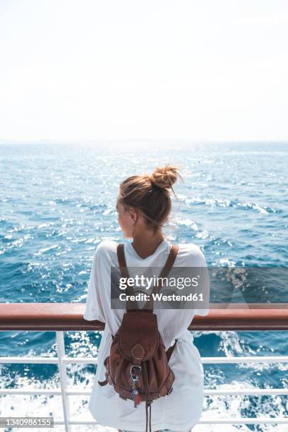 young woman wearing backpack looking at sea on boat during sunny day - fähre stock-fotos und bilder