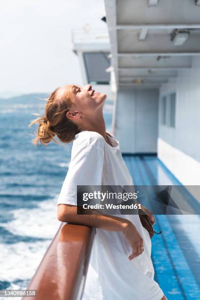 smiling woman with head back leaning on railing during summer in ferry boat - ferry photos et images de collection