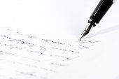 Black fountain pen is writing a letter or a manuscript on a white paper, copy space, close-up shot with selected focus