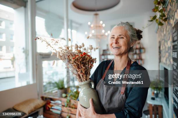 smiling female cafe owner holding flower vase in coffee shop - small businesses stock pictures, royalty-free photos & images