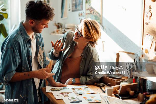 happy businesswoman discussing over sketches with male colleague at home office - illustrator stock pictures, royalty-free photos & images