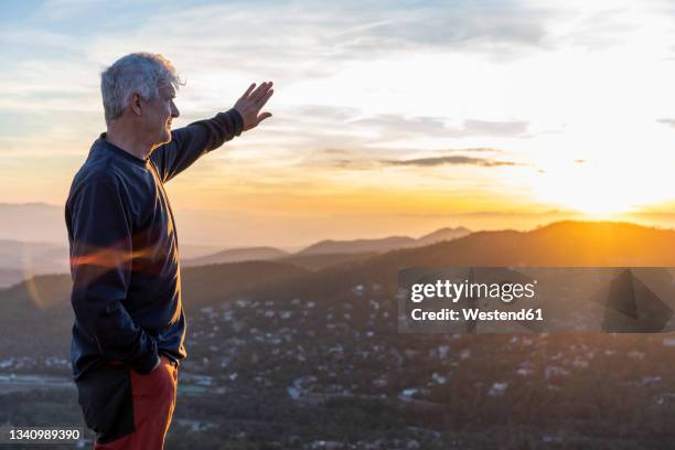 senior man shielding eyes while standing on mountain during sunset - barcelona free stock-fotos und bilder