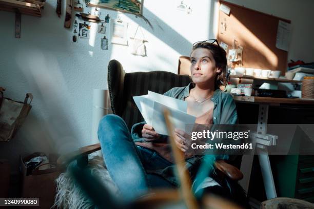 female professional sitting on chair holding sketch at home office - designer stock-fotos und bilder