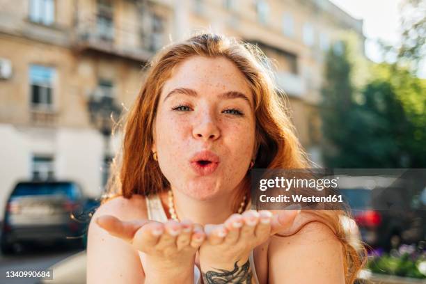 redhead woman gesturing while blowing kiss - kussmund stock-fotos und bilder