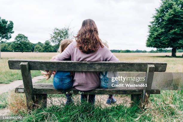 mother sitting with arms around daughters on bench - family with two children stock pictures, royalty-free photos & images