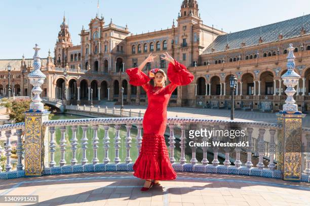 female flamenco artist dancing with hands raised at plaza de espana in seville, spain on sunny day - flamencos stock-fotos und bilder