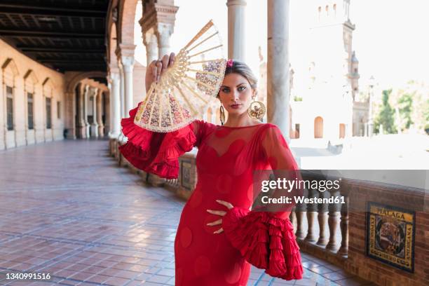 woman wearing traditional dress holding hand fan at plaza de espana walkway in seville, spain - seville dancing stock pictures, royalty-free photos & images