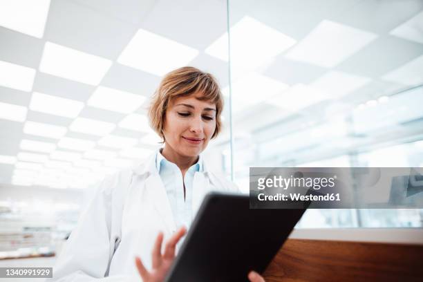 smiling female medical professional using digital tablet at pharmacy - female pharmacist with a digital tablet imagens e fotografias de stock