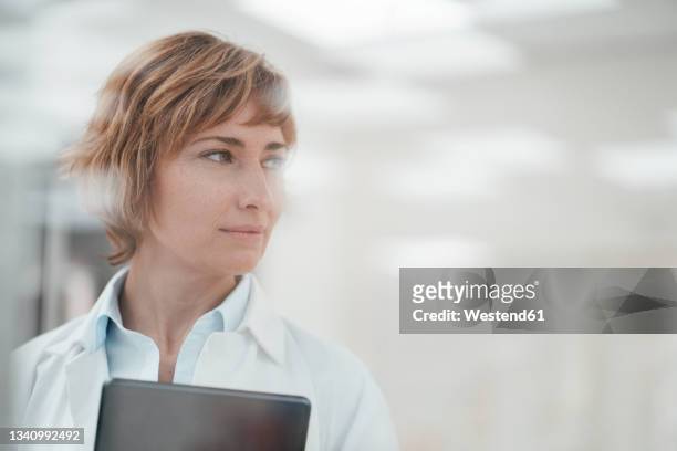 mature female expertise with digital tablet looking away at pharmacy store - female pharmacist with a digital tablet imagens e fotografias de stock