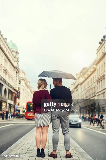 tiro de um jovem casal parado sob um guarda-chuva na cidade - back shot position - fotografias e filmes do acervo