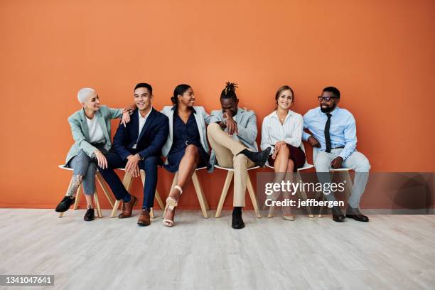 foto de un grupo de empresarios sentados sobre un fondo naranja - interview fotografías e imágenes de stock