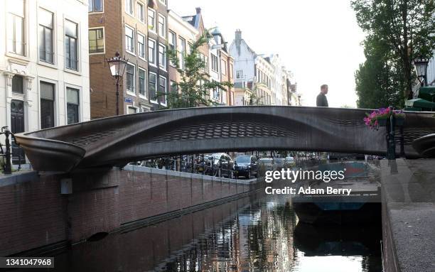 Pedestrian crosses a 12-meter 3D-printed, stainless steel bridge on September 17, 2021 in Amsterdam, Netherlands. The bridge, built by Dutch robotics...