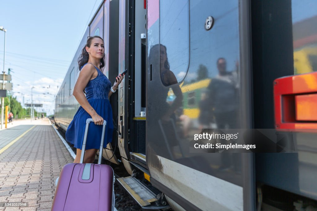 Woman checking mobile application before boarding a modern European train with a luggage on a sunny summer day.
