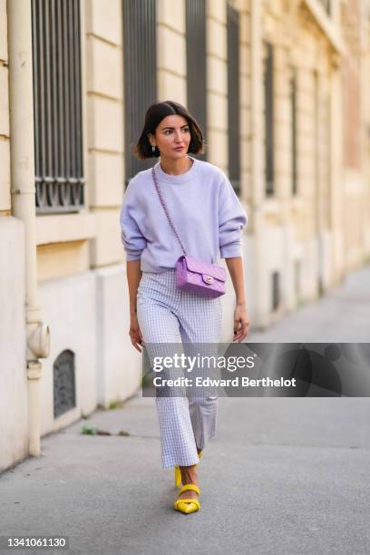 Alexandra Pereira wears silver and gold earrings, a pale purple fluffy wool pullover, pale purple and white checkered pattern large pants, a purple...