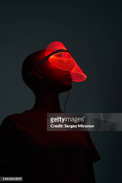 futuristic shot of young woman wearing led beauty mask with red lights over dark background - 3d face stock pictures, royalty-free photos & images