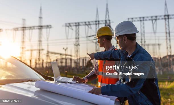 blue collar worker points towards sun setting over power distribution center with white collar worker looking the same direction. - power ストックフォトと画像