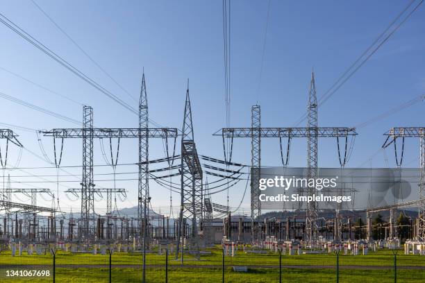 electricity distribution station from a power plant with poles and wires on a summer day with green grass and blue skies. - power mast stock pictures, royalty-free photos & images