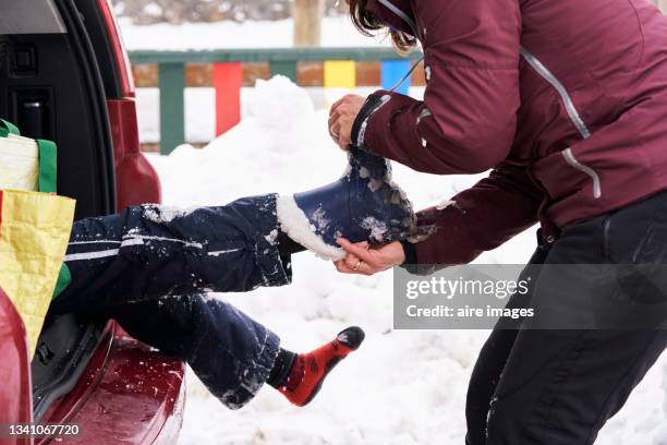 close up of lateral view of half body of mother removing snow boots her son - tira acessório - fotografias e filmes do acervo