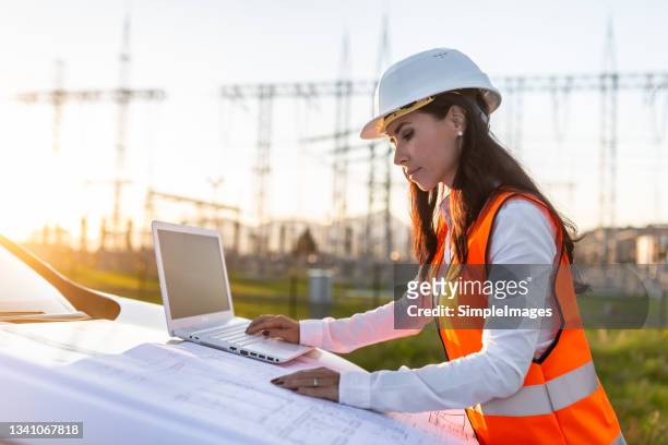 female manager checks a computer on a car hood next to a power station on a suny day. - airboard stock pictures, royalty-free photos & images