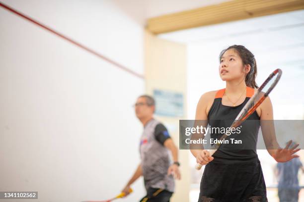 asian squash coach father guiding teaching his daughter squash sport practicing together in squash court - squash sport stockfoto's en -beelden