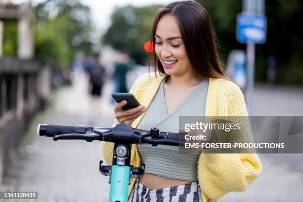 active, female student using her mobile phone in the city for renting a scooter - munich business stock pictures, royalty-free photos & images