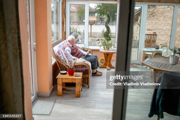 a senior man using a digital tablet while relaxing on the sofa at home - one senior man only stock pictures, royalty-free photos & images