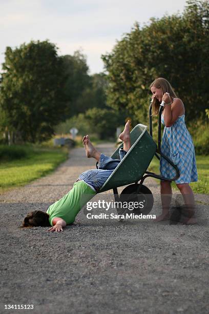 girl dumping woman of wheelbarrow - kruiwagen stockfoto's en -beelden
