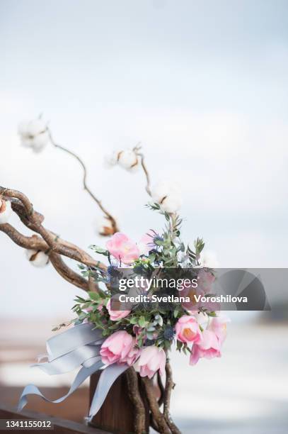 winter bouquet of tulips and blue thorns with sprigs of greenery and silver ribbons fluttering in the wind outdoors on the background of a wedding arch decorated with cotton balls and a blur winter lake covered with ice. - blumenstrauß tulpen stock-fotos und bilder