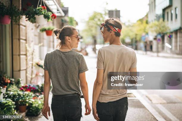 vista posteriore della coppia gay mentre cammina sul marciapiede e si guarda l'un l'altro - androgyn foto e immagini stock