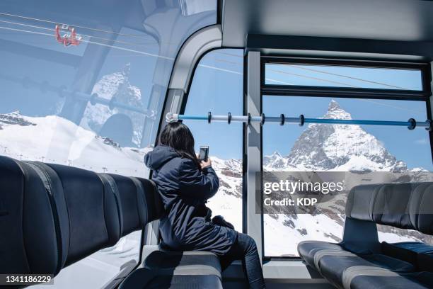 tourist woman having enjoy taking photos with her mobile phone while sitting in overhead cable car to the top of mountain. - teleférico veículo terrestre comercial - fotografias e filmes do acervo