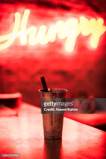 diner milkshake on a table, in front of a red neon hungry sign - americana metálica fotografías e imágenes de stock