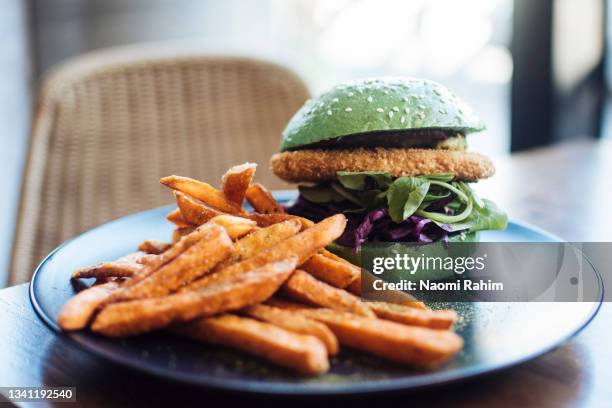 crumbed tofu burger in a green bun, with sweet potato fries - vegan food fotografías e imágenes de stock