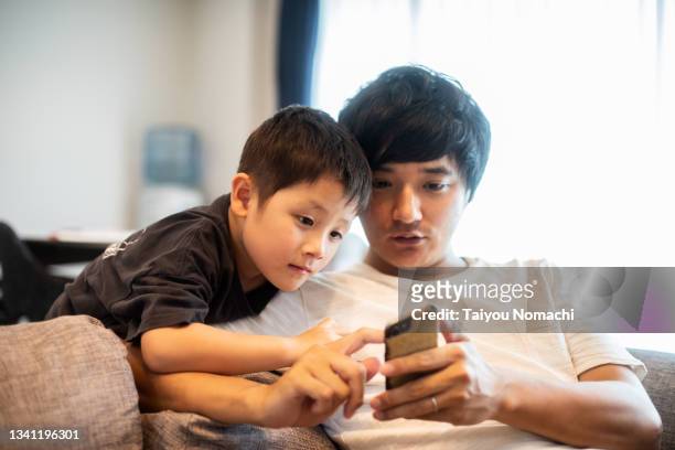 a father and his five-year-old son looking at their smartphones together - família de duas gerações imagens e fotografias de stock