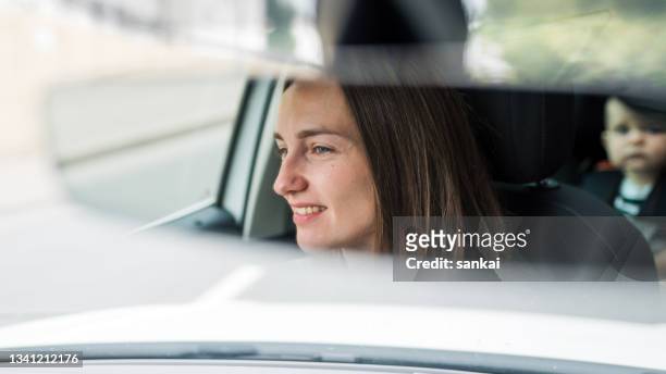 beautiful smiling woman driving a car with little baby on the backseat - rear view mirror stock pictures, royalty-free photos & images