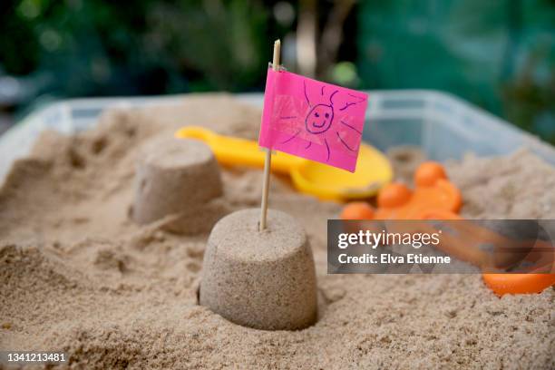 small sandcastle surrounded by sand inside a plastic sandbox and with a homemade flag from a pink sticky note with a drawing of a smiley face, put in the top - zandbak stockfoto's en -beelden